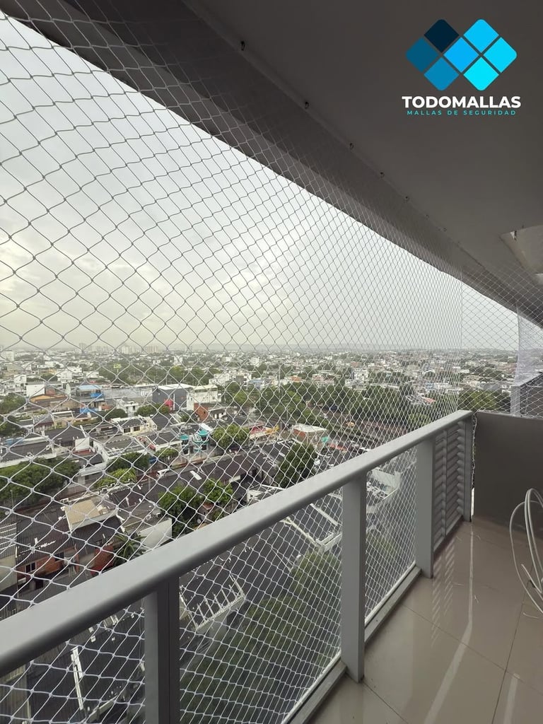 High-rise balcony with protective mesh netting overlooking a sprawling cityscape and green areas, featuring TODOMALLAS branding
