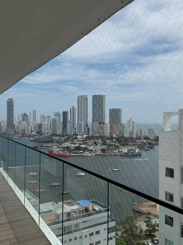 View of downtown city skyline with tall buildings and waterfront seen from a high-rise balcony with glass railing