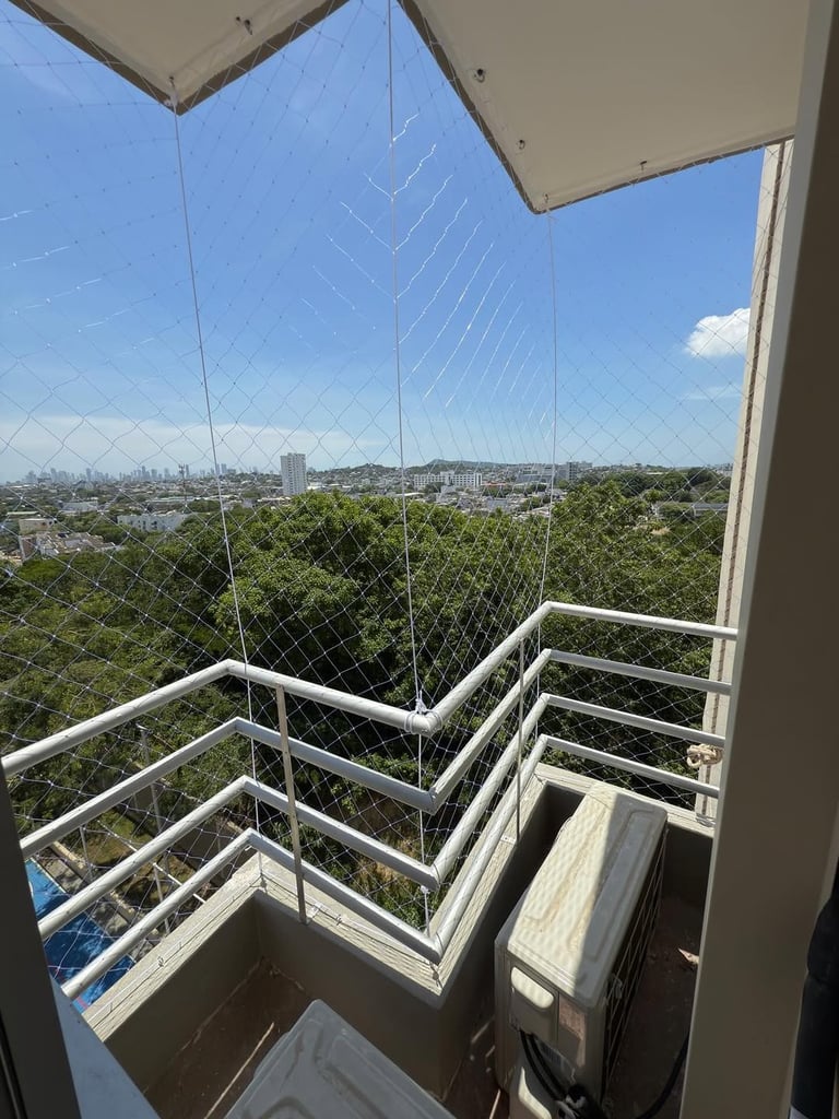 High-rise balcony with mesh safety netting overlooking cityscape with green trees and blue sky