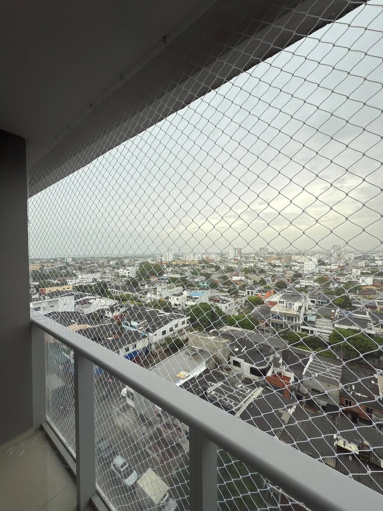 View from a high-rise balcony with protective mesh netting overlooking a sprawling cityscape with residential and commercial buildings