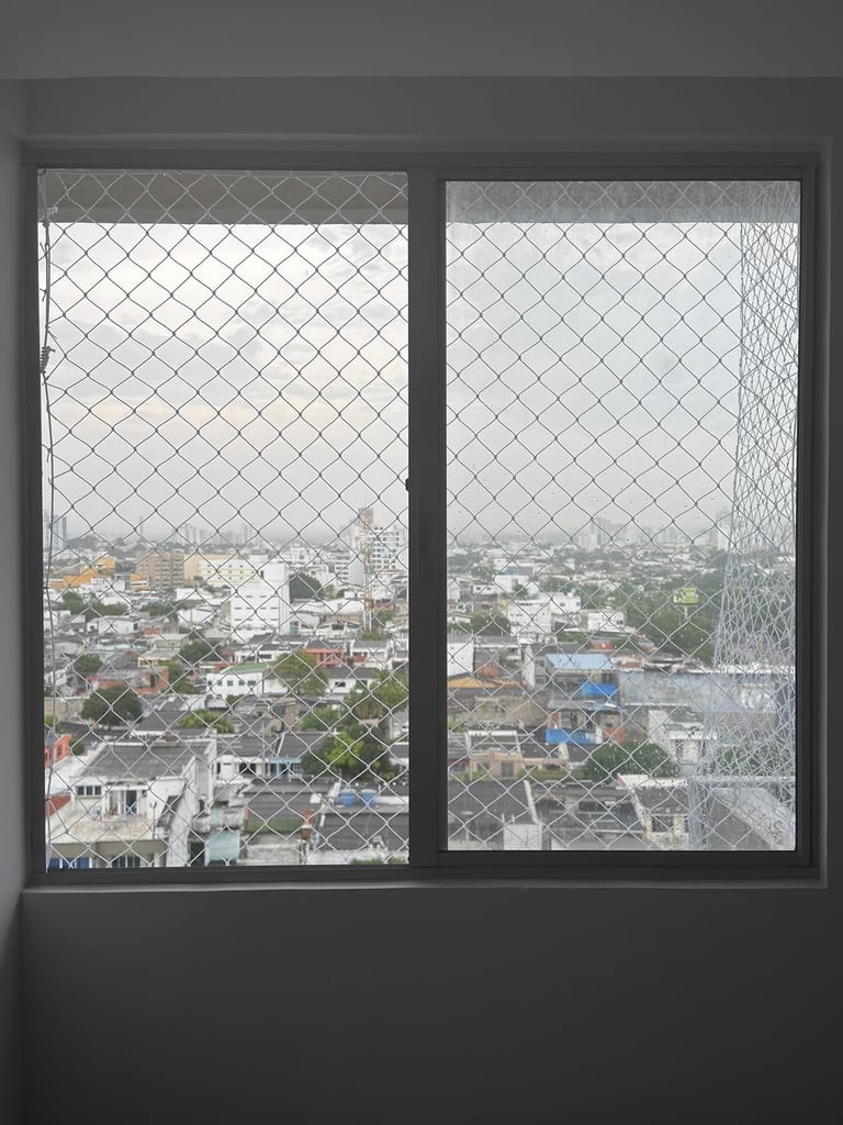 Window with metal mesh screen overlooking an urban cityscape with residential buildings and green vegetation