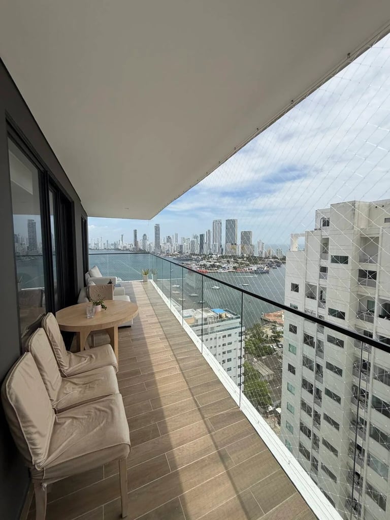 High-rise apartment balcony with seating overlooking a city skyline and waterfront bay