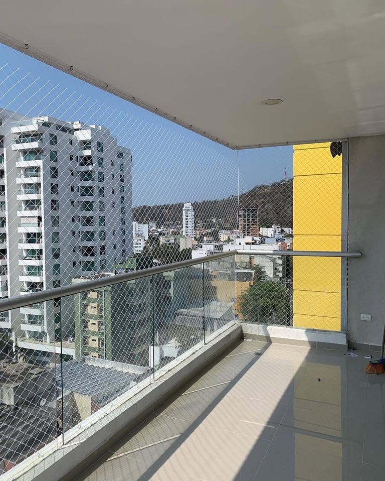 Modern apartment balcony with mesh safety net, metal railing, and yellow shade panel overlooking urban cityscape with mountains